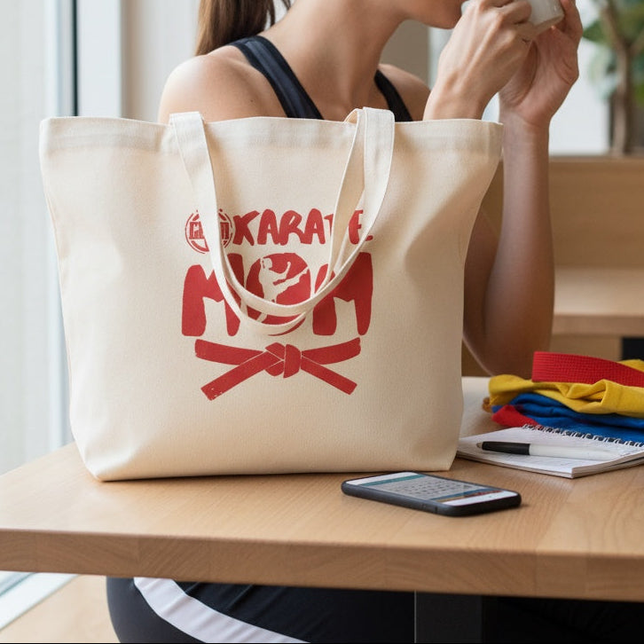Woman sitting at a table with a tote bag labeled 'Karate Mom' holding a cup.