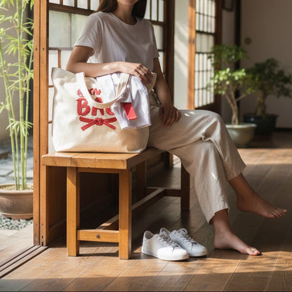 Woman sitting on a wooden stool holding a tote bag with text in a room with wooden floors and plants.