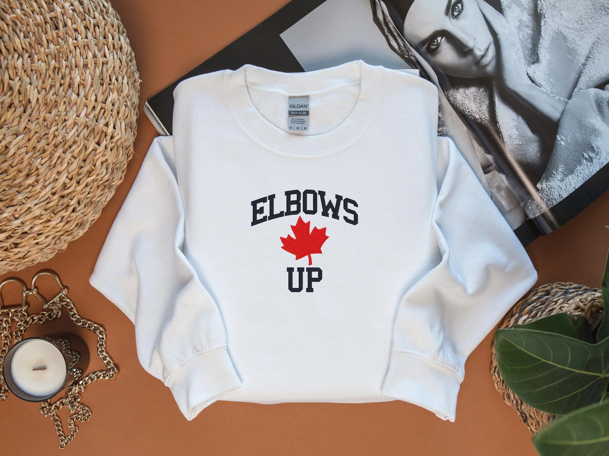 White sweatshirt with 'ELBOWS UP' text and red maple leaf on a brown surface.